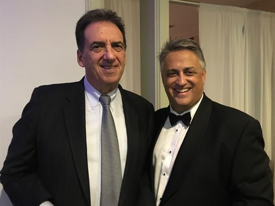 Two men wearing tuxedos enjoy each other's company during a formal gathering.