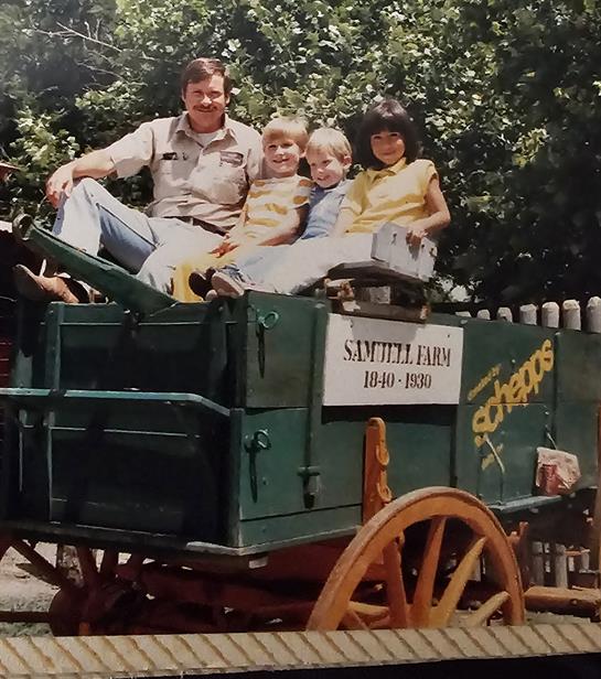 A family gathers atop a vintage wagon, smiling and enjoying their time together at a farm.