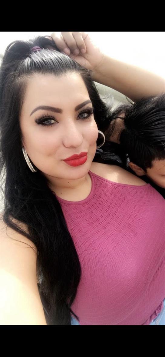 A woman takes a selfie with bold makeup, as a child leans in behind, smiling.