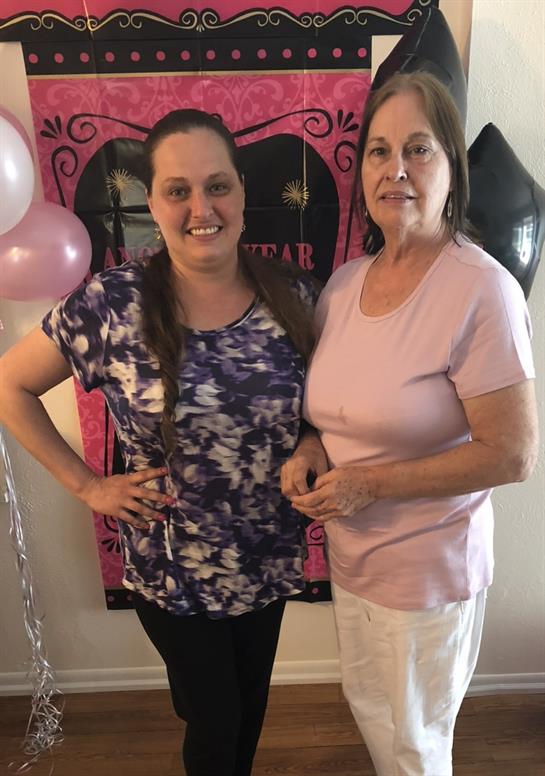 Two women stand together smiling in front of colorful decorations at a lively birthday gathering.
