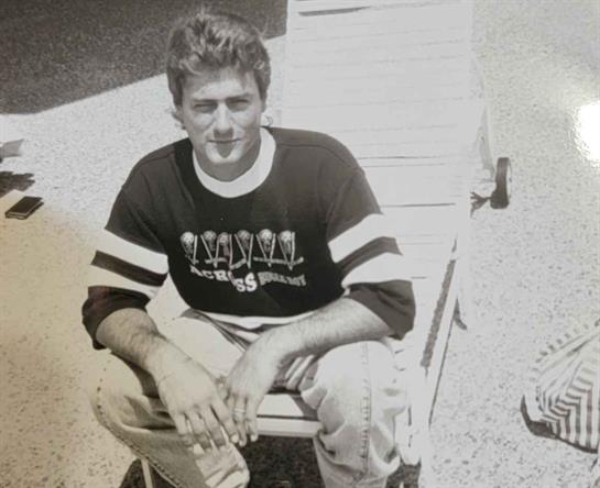 A young man sits comfortably in a deck chair, enjoying the warm sunlight with a relaxed demeanor.