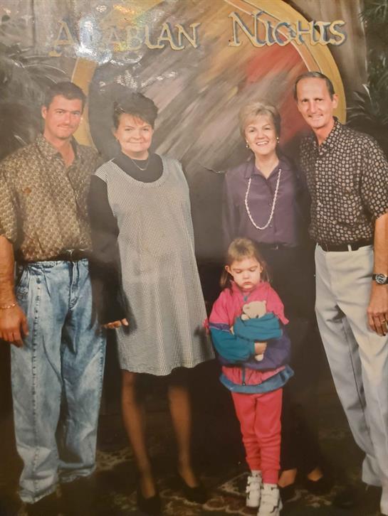 A group of five people dressed smartly stands together, celebrating a joyful occasion.