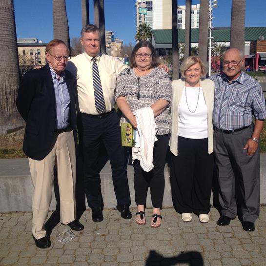 A group of five friends stands together outdoors, smiling and enjoying their time in the sun.