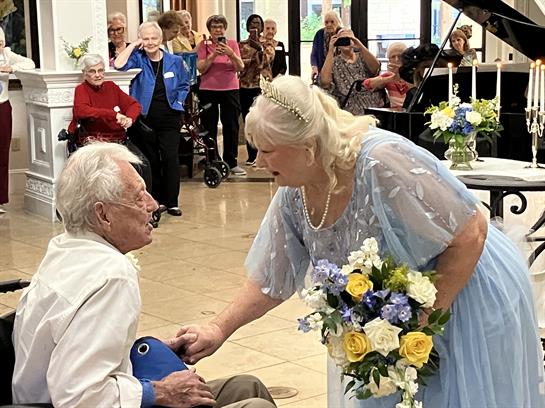 An elderly couple enjoys a touching interaction at a lively community event, surrounded by guests.
