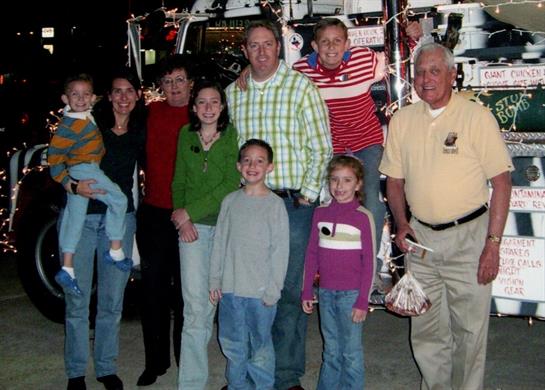 A group of family members poses joyfully together next to a brightly decorated vehicle.