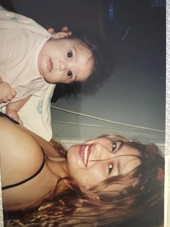 A joyful mother embraces her baby with a warm smile in a comfortable indoor space.