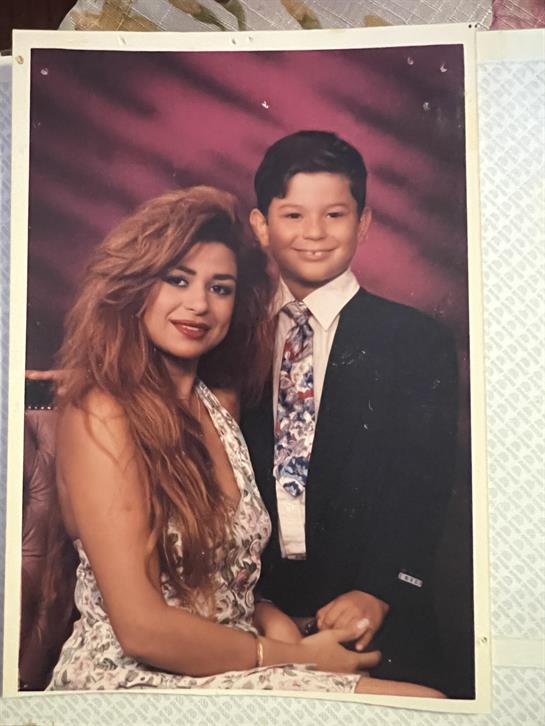 A mother and her son are smiling while dressed elegantly in a studio setting.