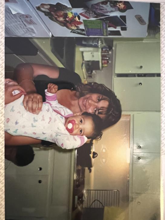 A loving mother cradles her happy baby in a warm kitchen setting filled with family warmth.