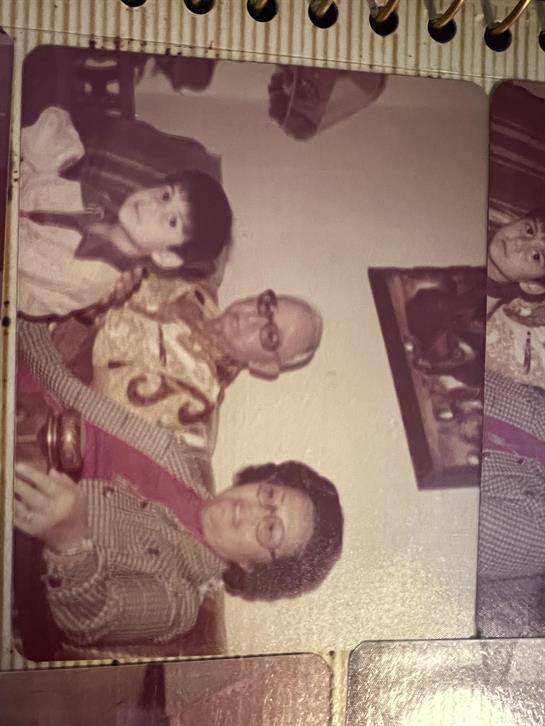 Three family members, including a child, pose happily in a warm home environment.