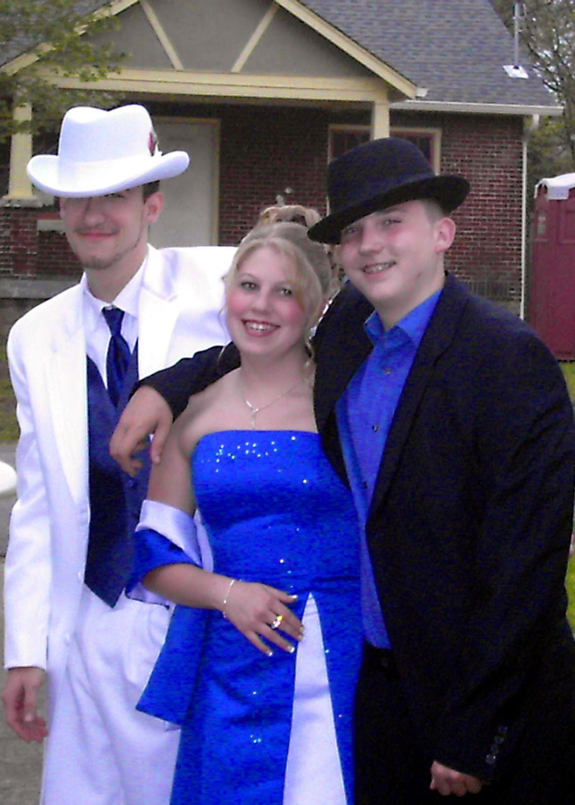 Three friends pose together, showcasing their formal outfits in a festive atmosphere outside.