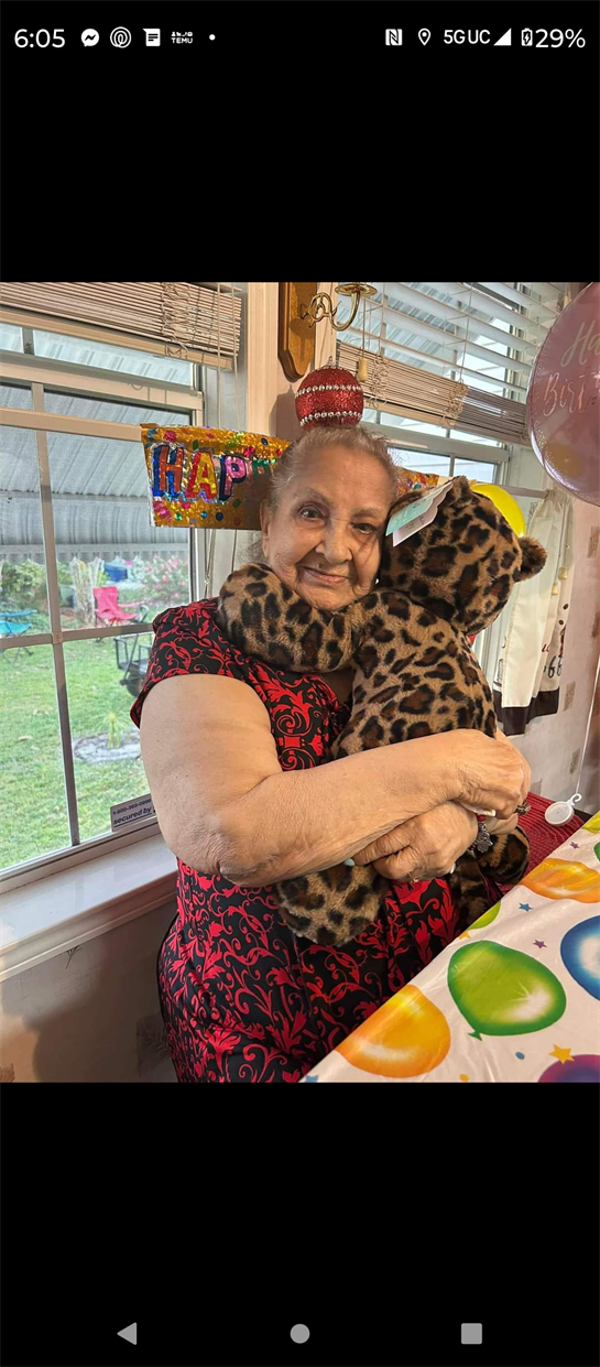 Happy elderly woman holds a stuffed animal in a festive setting, surrounded by colorful decorations.