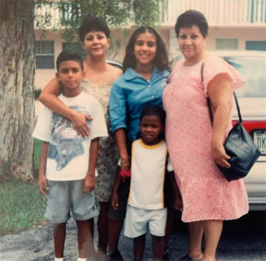 Five family members pose together, smiling outside in a residential neighborhood.