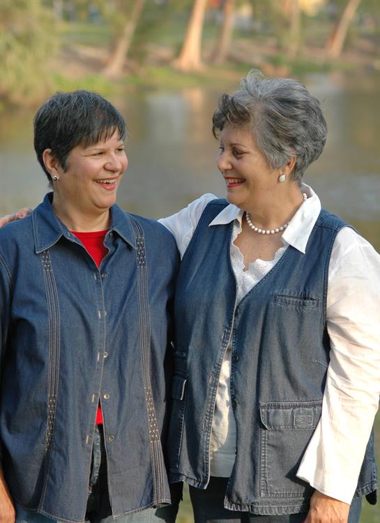 Two close friends smile and laugh together near a peaceful lake surrounded by trees.
