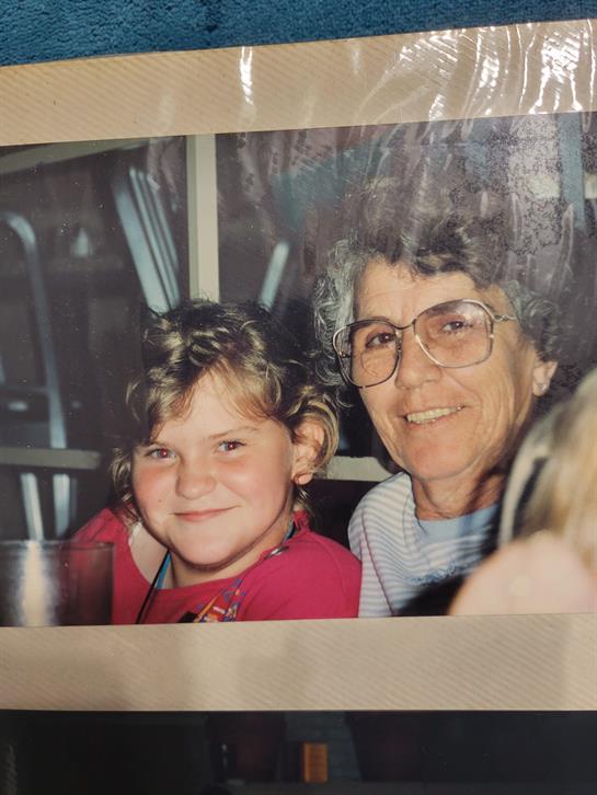 A young girl and her grandmother smile happily while sitting together at a family event.