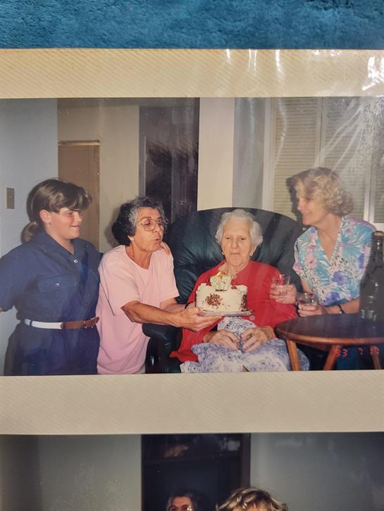 Four family members are joyfully celebrating a birthday with an elderly woman as she holds a cake.