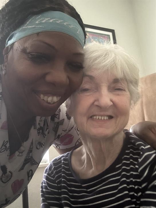 Caregiver and elderly woman joyfully pose together in a nursing home during a friendly visit.
