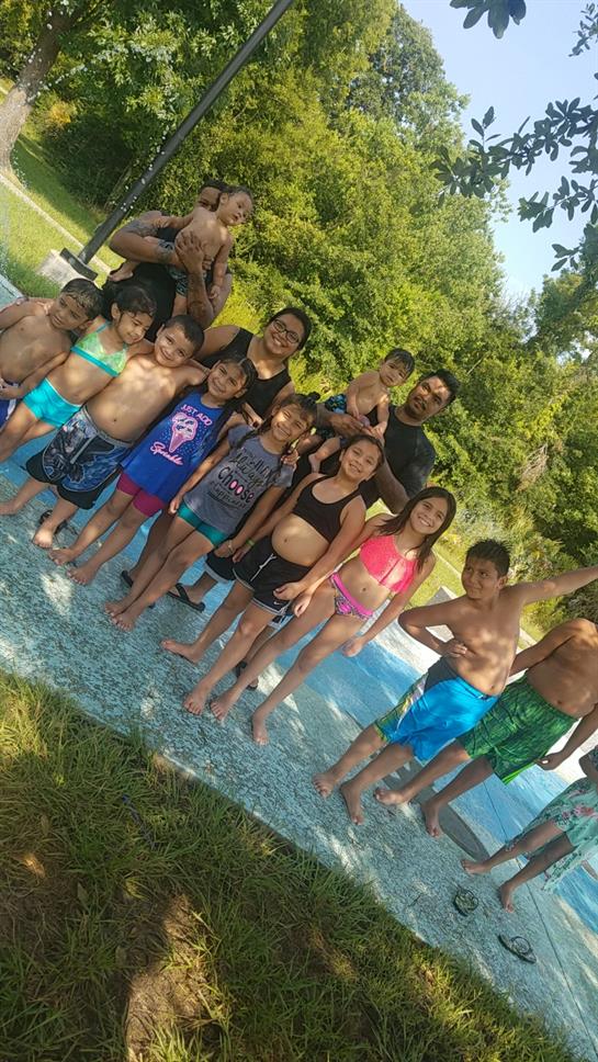 Kids and adults gather around a swimming pool, smiling and playing together on a sunny day.