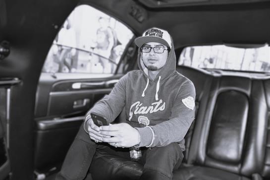 Individual is seated inside a black car, focused on his smartphone as city life unfolds outside.