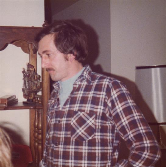 A man wearing a plaid shirt interacts with friends in a cozy living room setting.