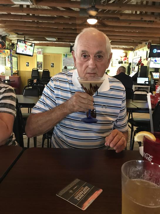 Older gentleman sips a colorful cocktail while seated at a restaurant table.