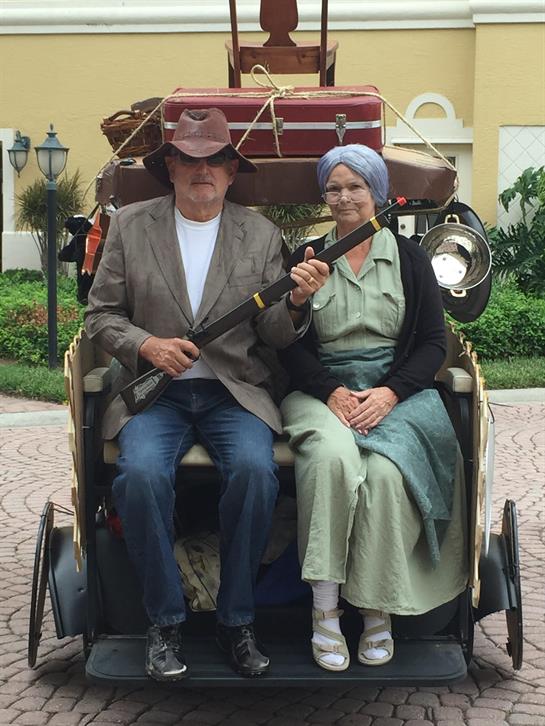 An elderly couple relaxes in a classic carriage while dressed in traditional attire.