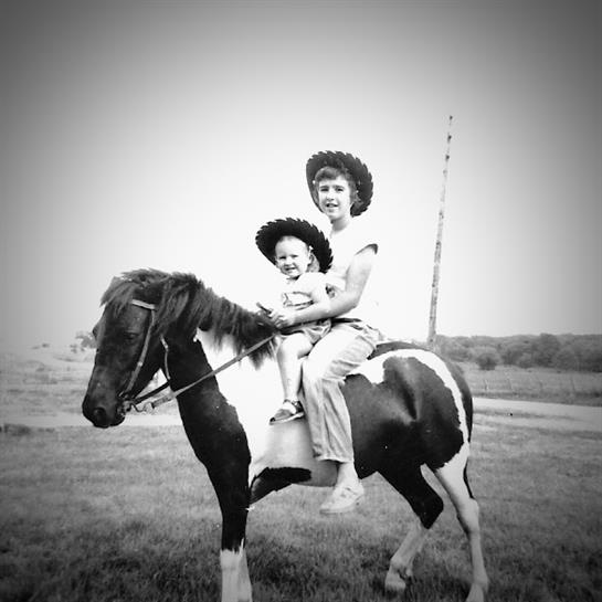 Two individuals wear matching hats as they joyfully ride a horse together outdoors.