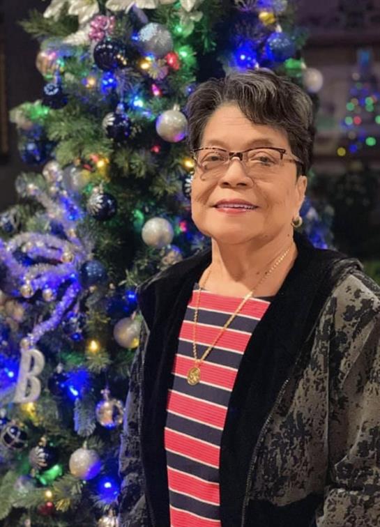 A woman stands cheerfully beside a vibrant Christmas tree filled with blue and silver decorations.