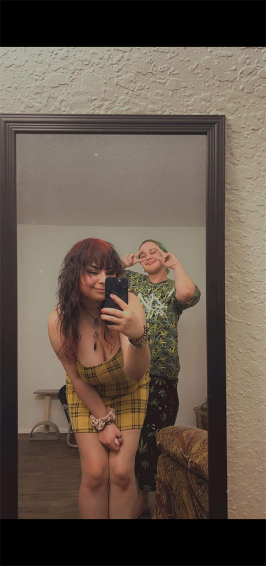 Two friends are having a good time, posing playfully in front of a mirror with smiles.