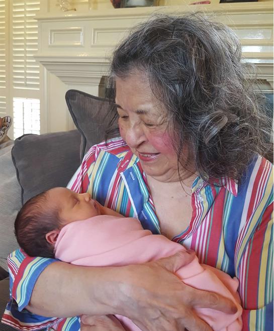 A grandmother smiles tenderly as she holds her newborn granddaughter swaddled in pink.