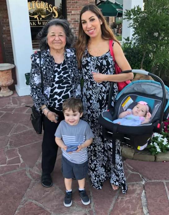 Three family members happily pose outside with two young children on a beautiful day.