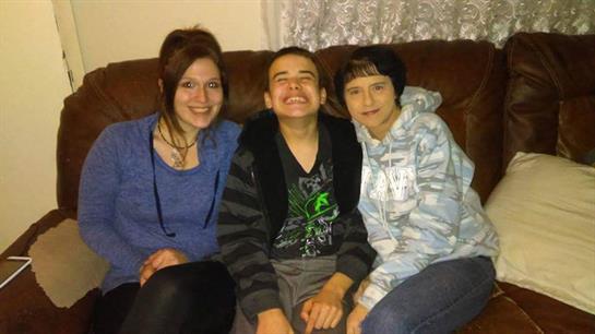 Three individuals share smiles while sitting on a couch in a relaxed home environment.