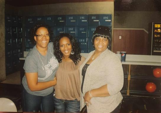 Three women share laughter and joy at a social gathering in a lively setting.