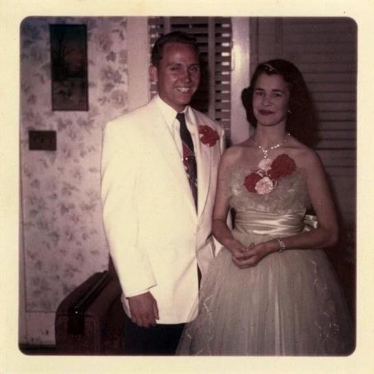 A man and woman pose together in formal wear, surrounded by a charming vintage decor.