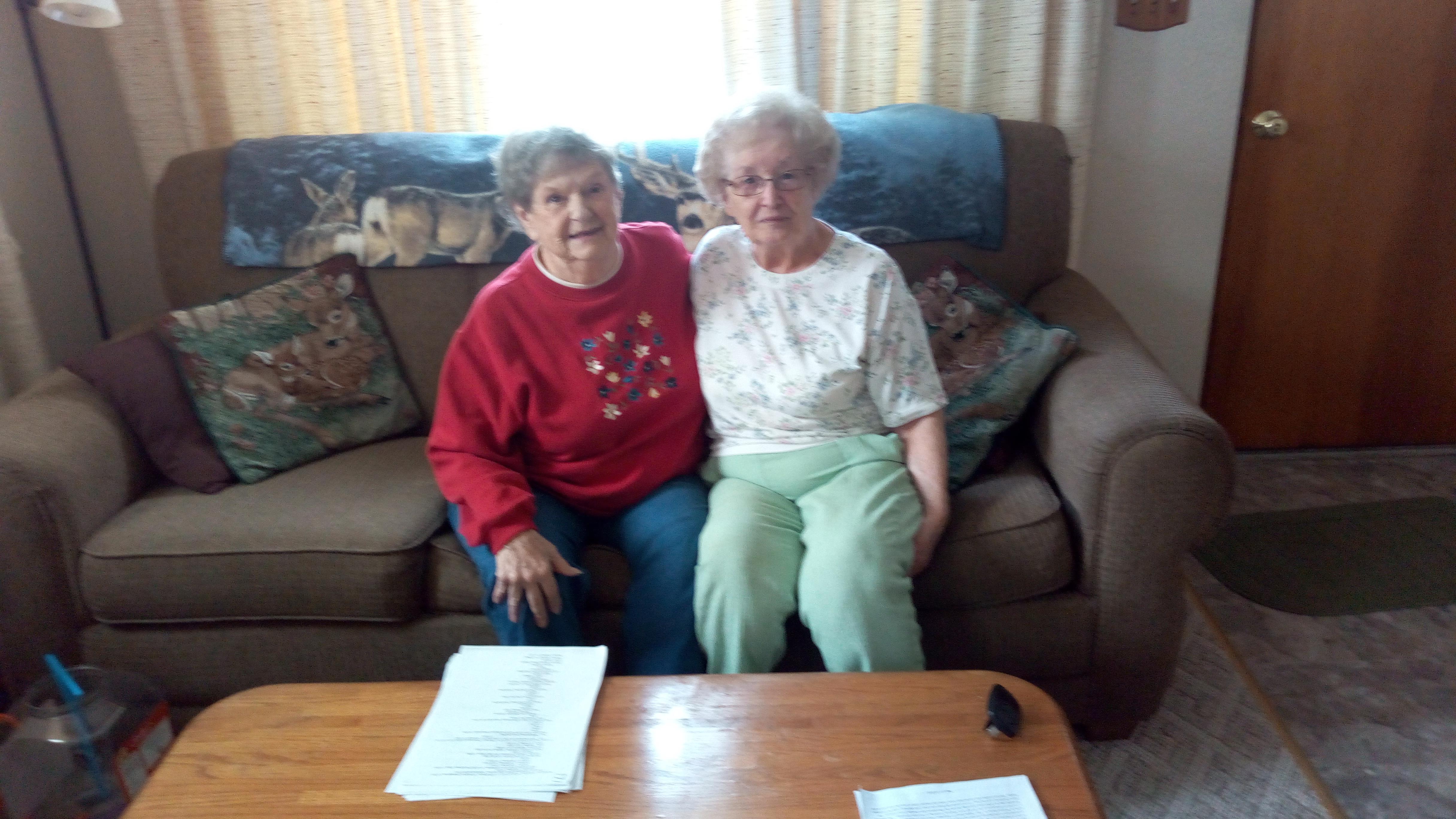 Two friends enjoy each other's company on a comfortable couch in a well-lit living room.