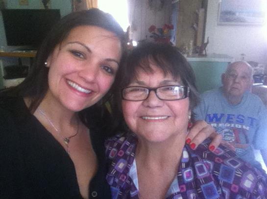 Two women smile brightly together while an older man looks on in a cozy living room.