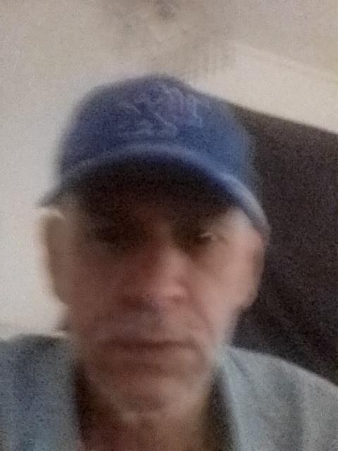 A man in a blue cap is seated indoors, his expression suggests deep thought or reflection.
