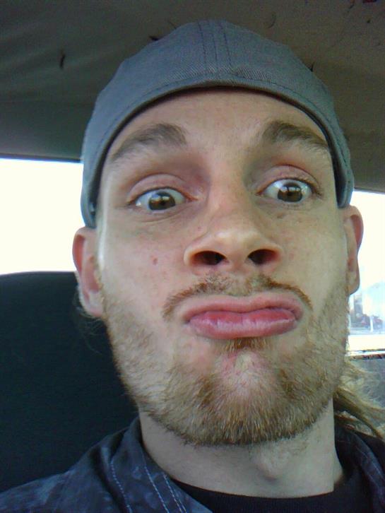 A young man with a hat is humorously contorting his face inside a vehicle.