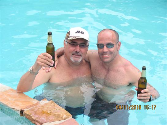 Two men are having a good time in a pool, smiling and holding up beer bottles together.