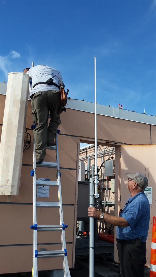 Two workers are using a ladder to install equipment on a rooftop during daytime.