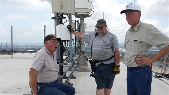 Technicians collaborate on rooftop tasks, assessing equipment under a clear sky.