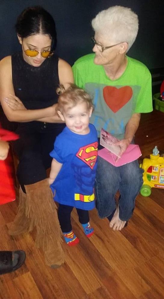A happy child in a superhero costume enjoys time with two adults.