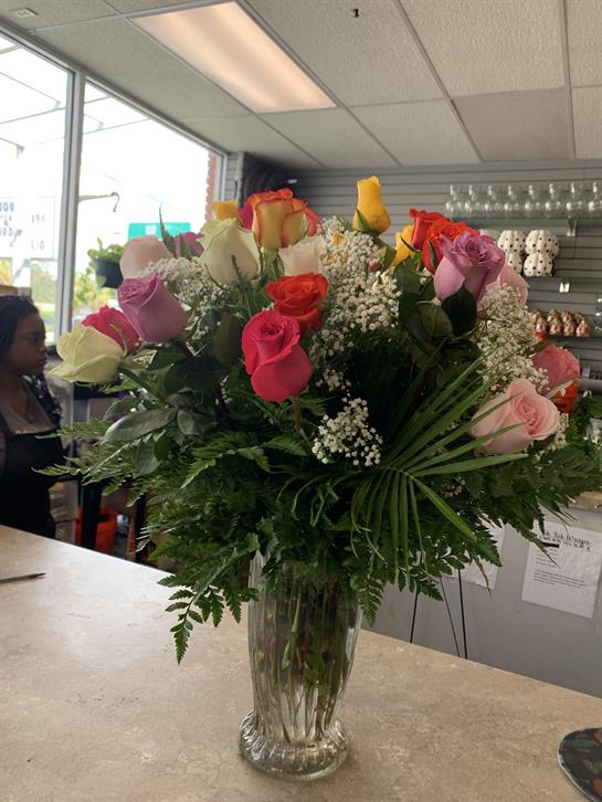 Vibrant bouquet features various colored roses in a clear vase at a busy flower shop.