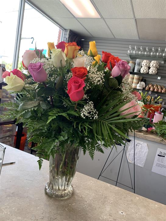 A vibrant arrangement of roses in various colors is displayed on a counter in a floral shop.