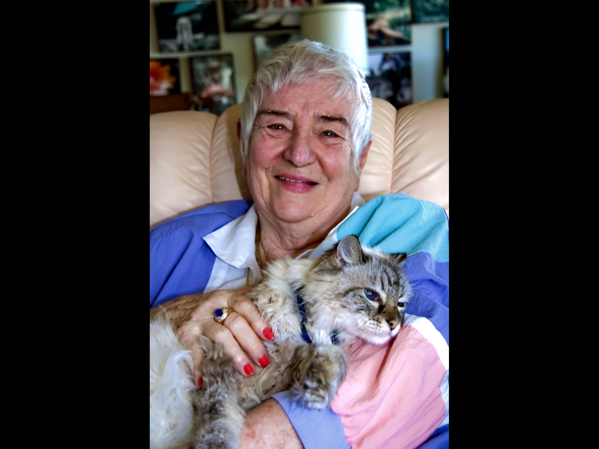 A senior woman smiles happily, gently holding her cat in a cozy living room setting.