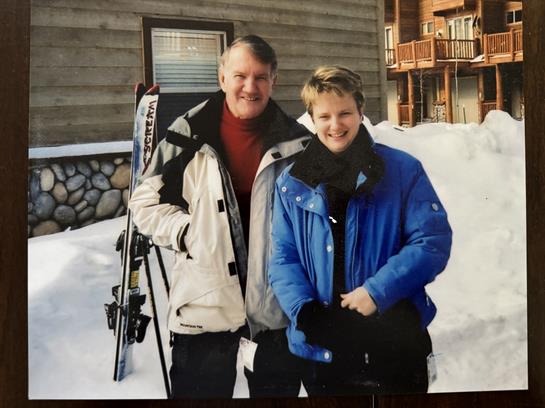 Two friends stand outside a mountain lodge, wrapped in warm clothing, enjoying winter activities.