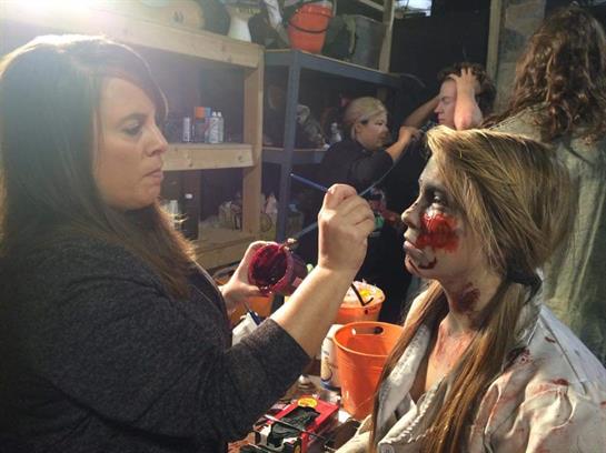 A makeup artist enhances a model's look with special effects for Halloween celebrations.