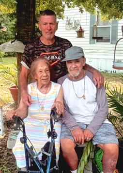 Three family members enjoy a sunny afternoon in a garden with greenery and a friendly atmosphere.