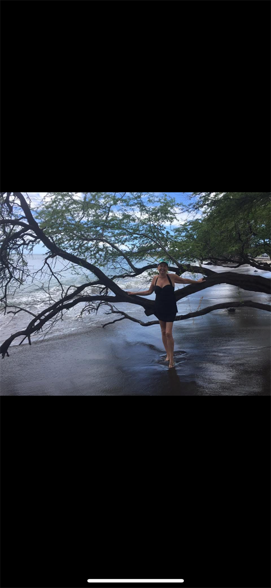 A woman gracefully poses on a tree branch overlooking a tranquil beach with gentle waves.