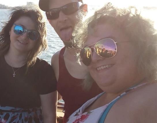 Three friends are posed together, smiling and enjoying the sunny weather by the water.