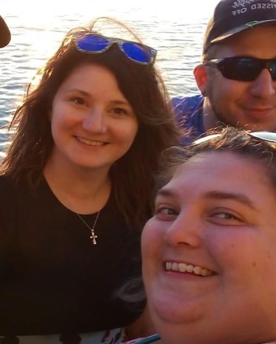 Friends smile happily together by the waterfront as the sun sets, capturing a joyful moment.